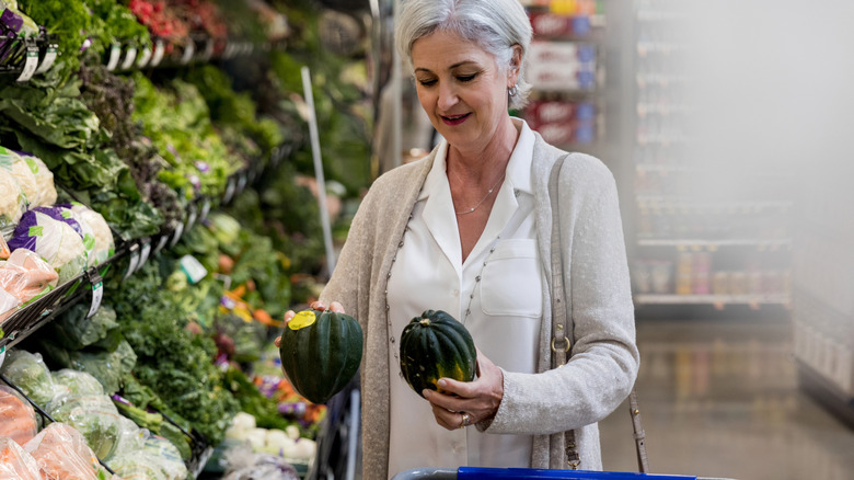 woman holding an acorn squash in each hand in store