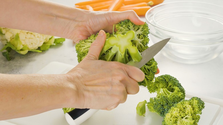 Hand slicing raw broccoli with knife