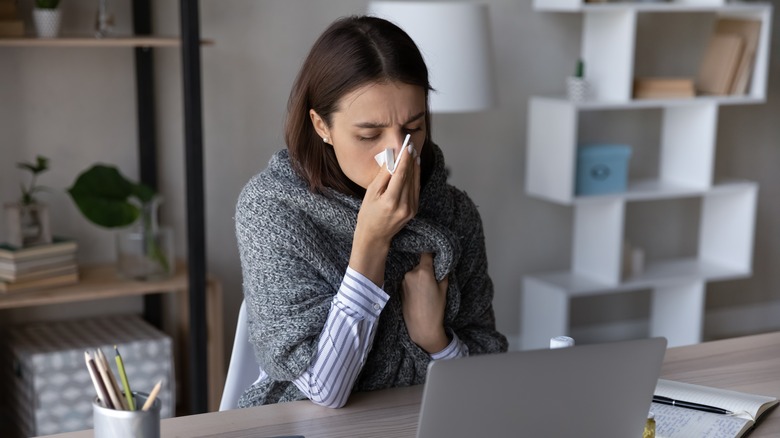 Woman blowing her nose at her desk