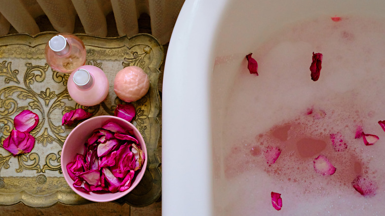 Bath bomb next to flower petals and bathtub 