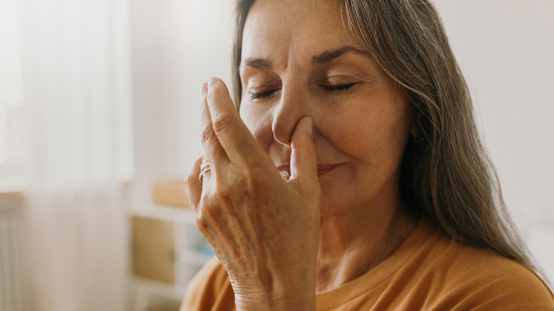 Older woman closing her eyes and holding one nostril closed