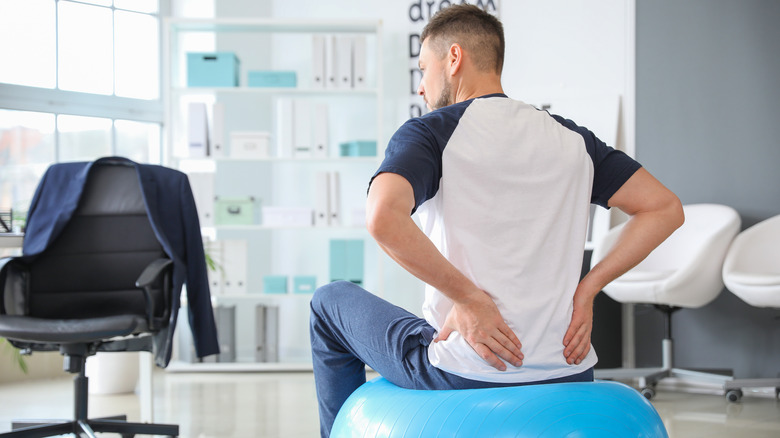 Man having low back pain while sitting on a Swiss ball