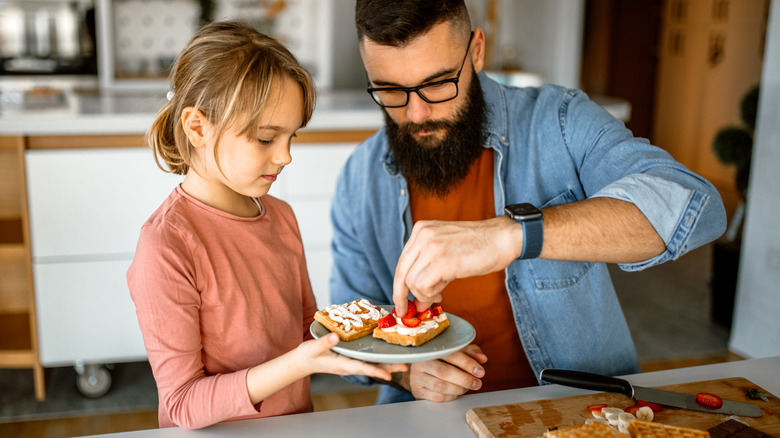 father and daughter topping waffle with fruit