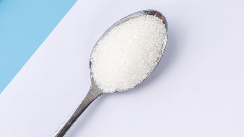 Teaspoon of sugar on white surface