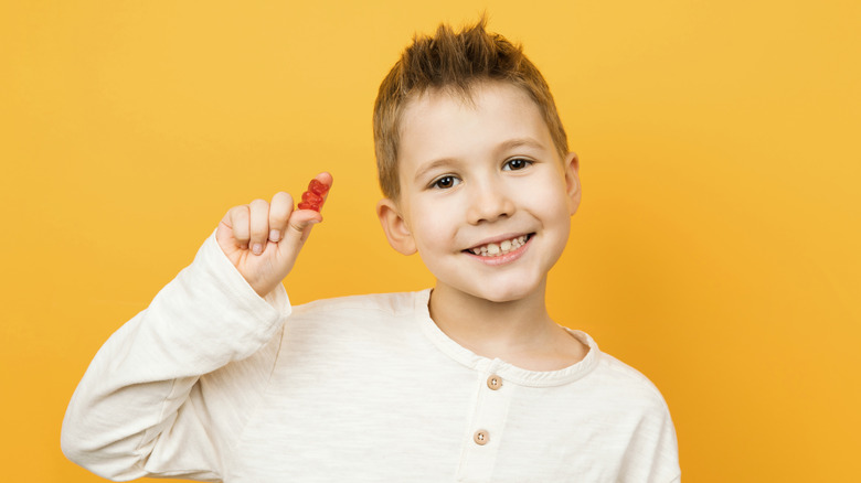 boy holding a gummy vitamin on yellow background