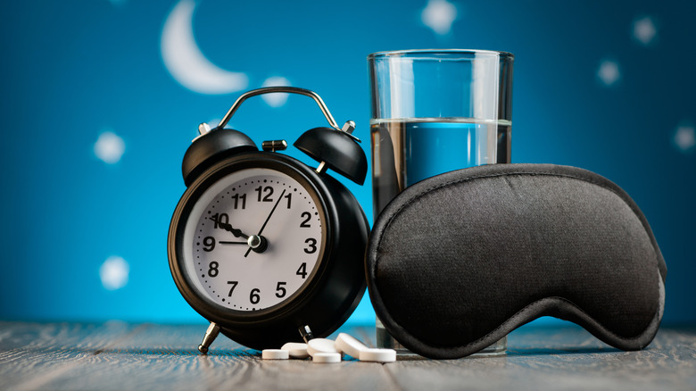 black clock, sleeping mask, and pills on starry background