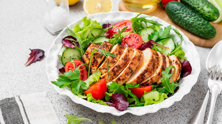 A healthy salad with grilled chicken and tomatoes sits on a table
