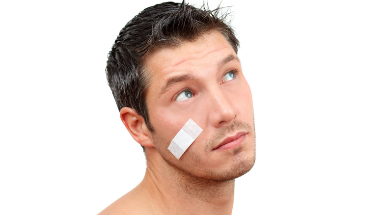 Man wearing white bandaid on his cheek, appearing against a white background