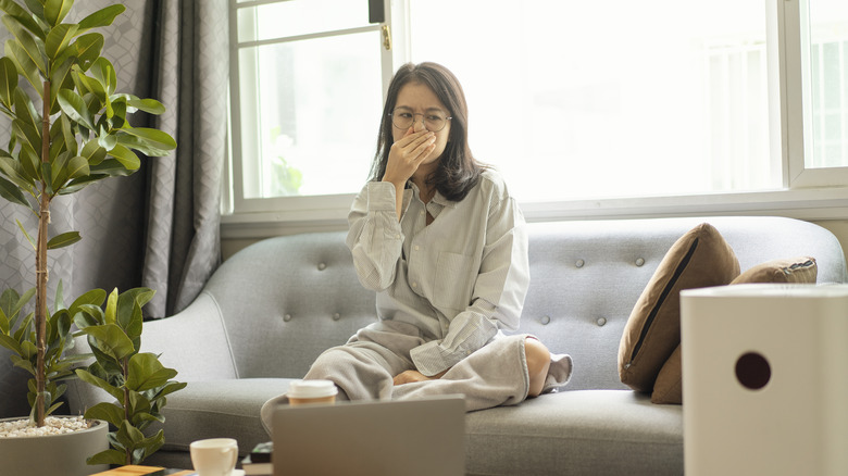 woman holding her hand over her nose and mouth while sitting on the couch