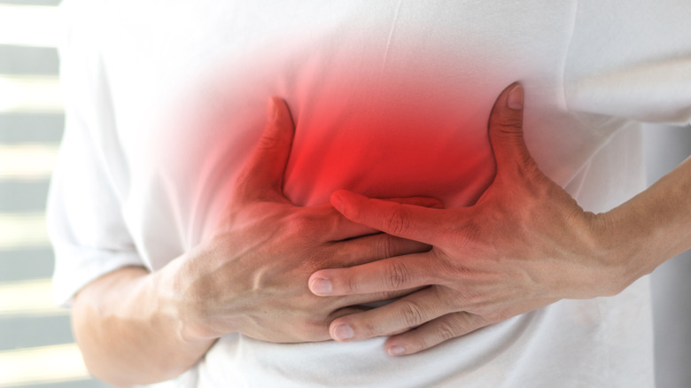 man in white shirt holding hand on chest highlighted in red signifying pain