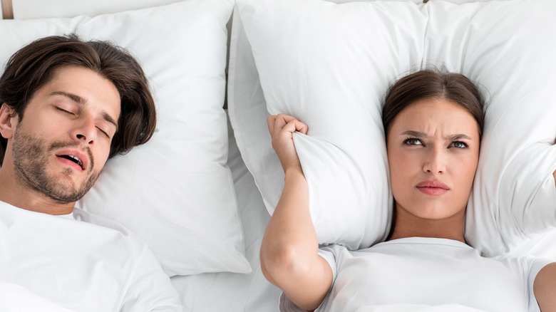 man asleep with woman covering ears with pillow in bed