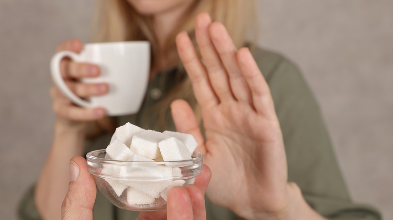 female holding coffee cup with hand in stop position refusing sugar cubes