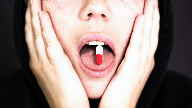 teenager with open mouth, hands on her cheeks and pill on her tongue 