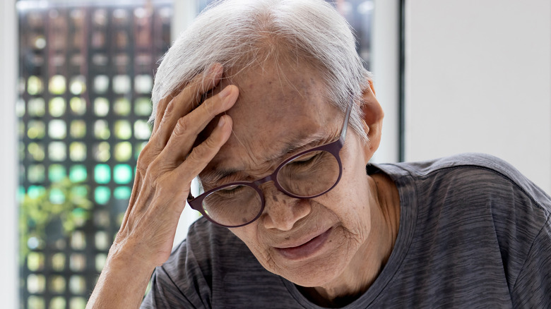 elderly asian man holding head appearing distressed