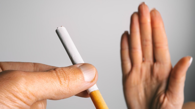 male hand holding cigarette with female hand displaying stop