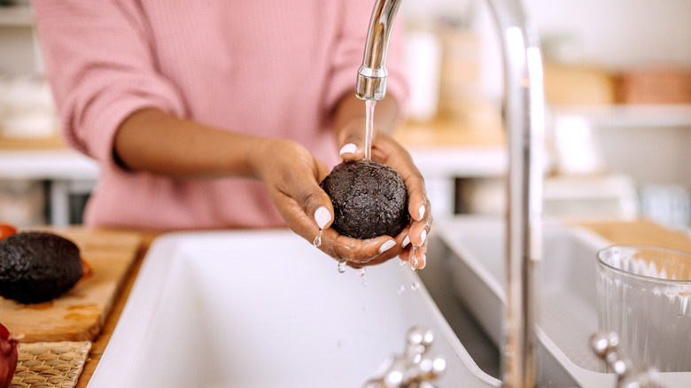 Woman's hands washing avocado in sink