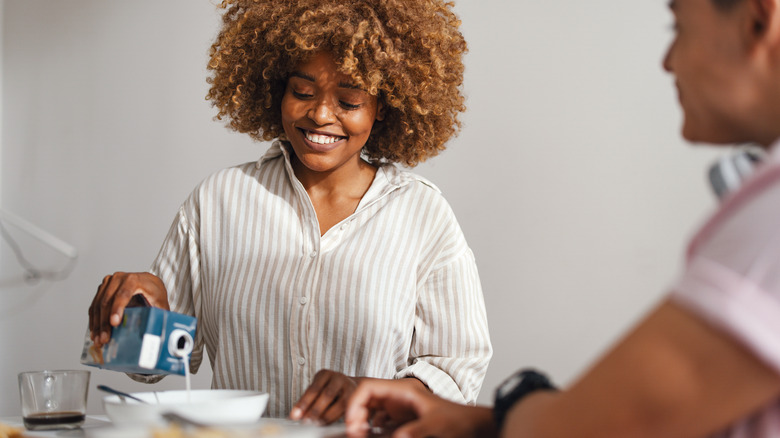 Smiling woman pouring milk in bowl