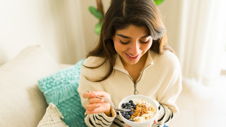 Smiling woman eating bowl of fruit and oats