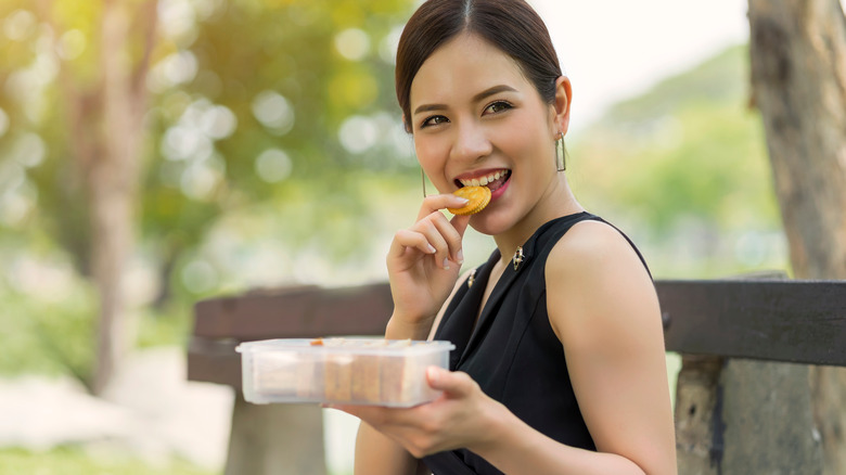 woman eating peanut butter and crackers on a park bench