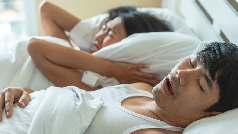 Man snoring in bed with frustrated partner
