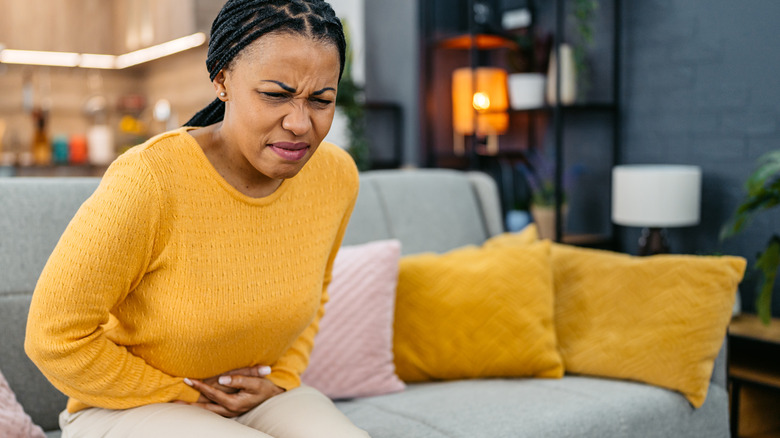 woman sitting on sofa holding stomach in discomfort