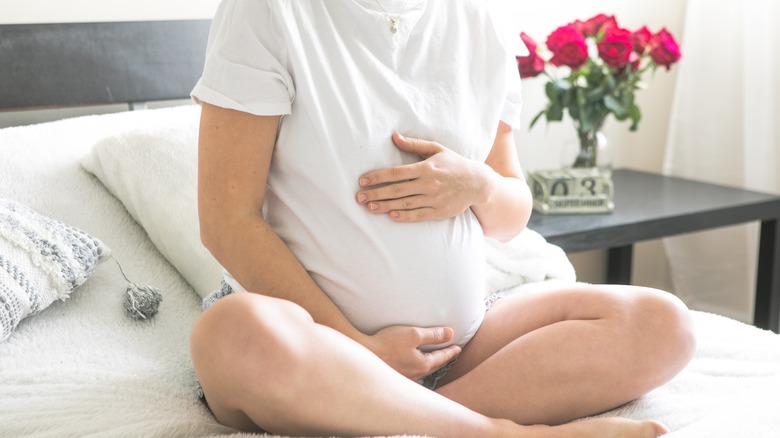 Pregnant woman sitting in bed holding her belly