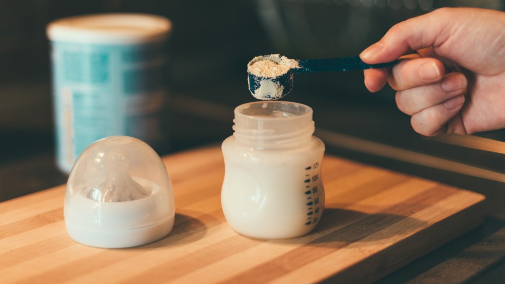 Hand measuring baby formula into milk bottle