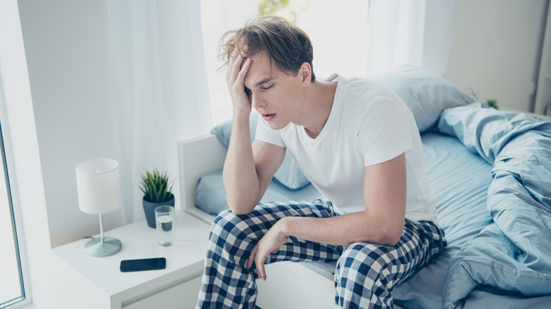 A man is sitting in his bed very tired