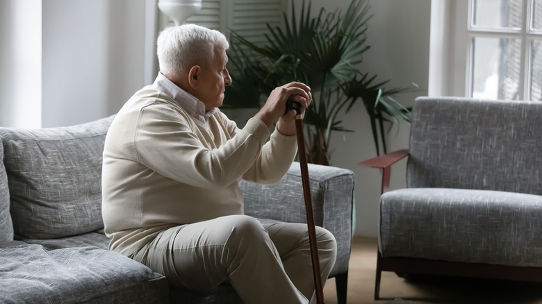 unhappy older man seated on couch with cane