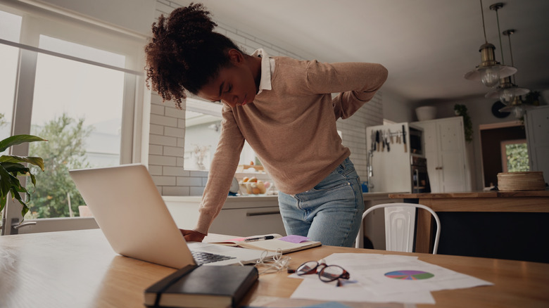 woman standing over desk, holding back