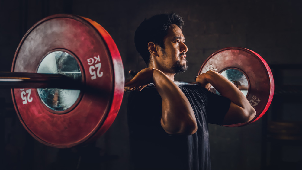 A man holds a barbell in front of his chest on his shoulders