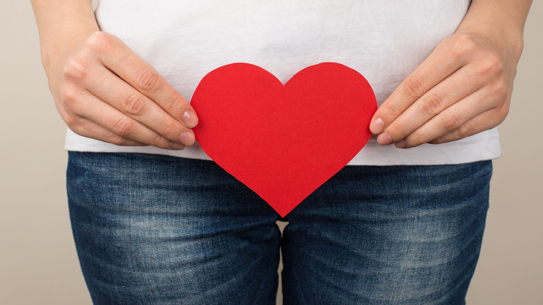 woman holds red heart over crotch