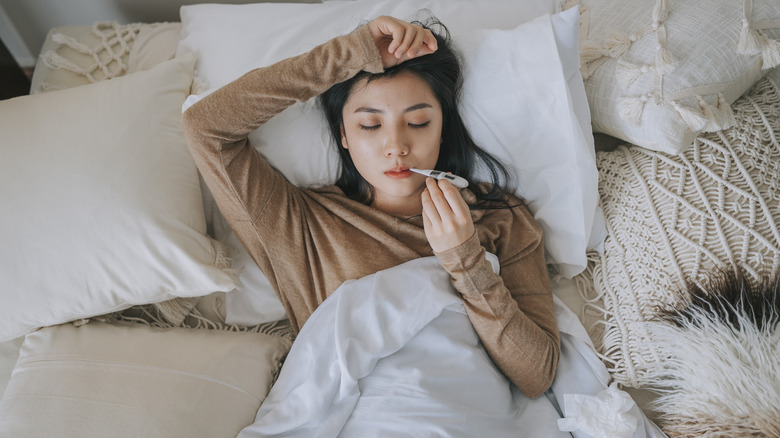 Woman lying in bed with thermometer in mouth
