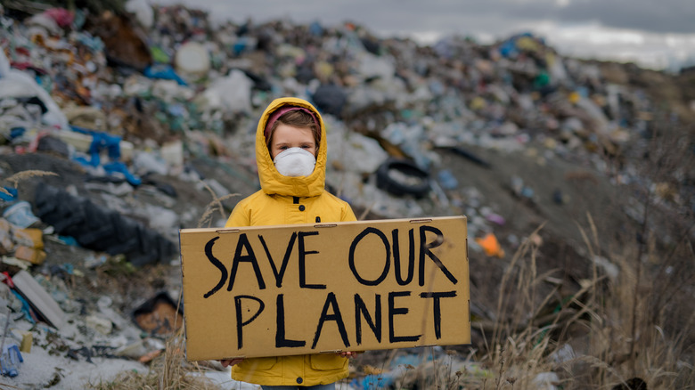 child holding "save our planet" placard in front of landfill