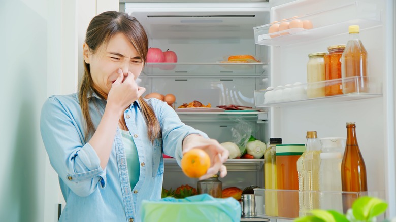 young Asian woman tossing smelly food from fridge