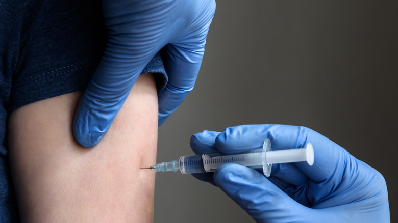 Pair of gloved hands administering vaccine into arm of patient