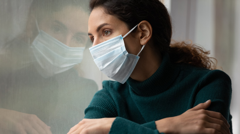 woman with mask looking out window