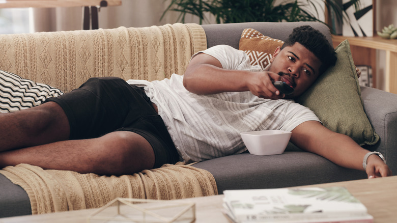 Man laying on couch holding TV remote