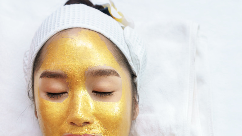 a young asian woman with a gold face mask smiling against white backdrop