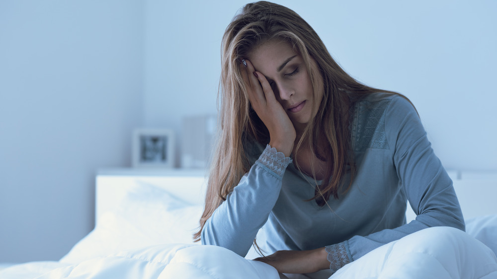 Stock photo of groggy young woman sitting up in bed