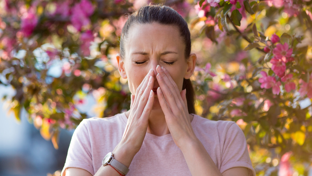 woman sneezing in front of a blooming tree