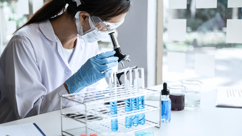 Scientist in lab coat looks through microscope in laboratory