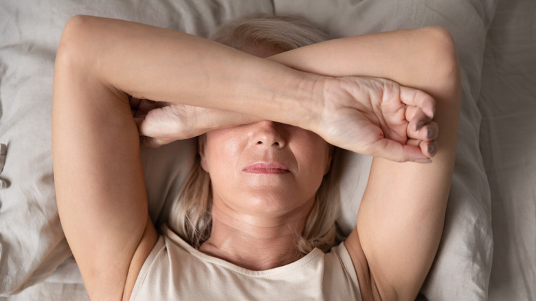 woman with arms over eyes in bed