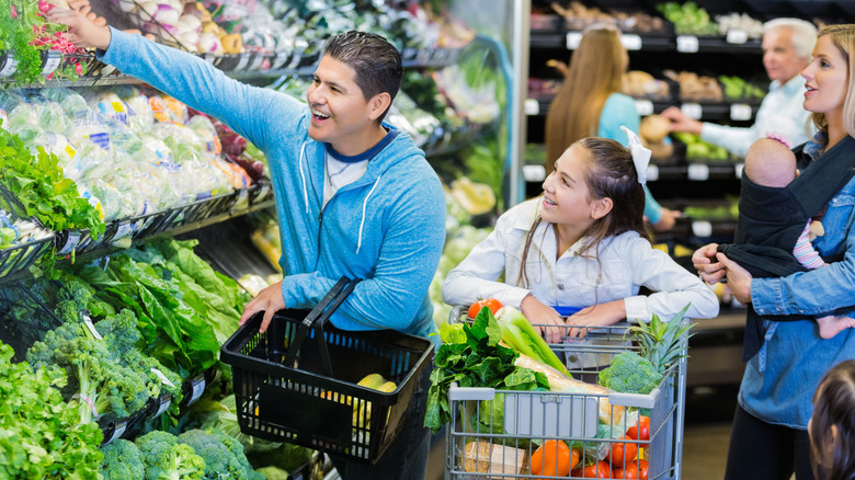 parents shopping for vegetables with child and baby