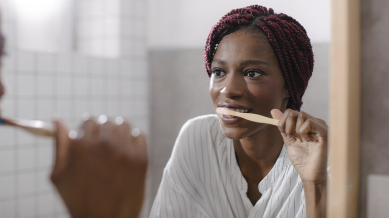 Woman brushing teeth in bathroom mirror