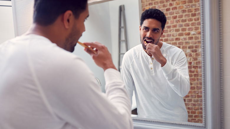 Man brushing teeth in mirror