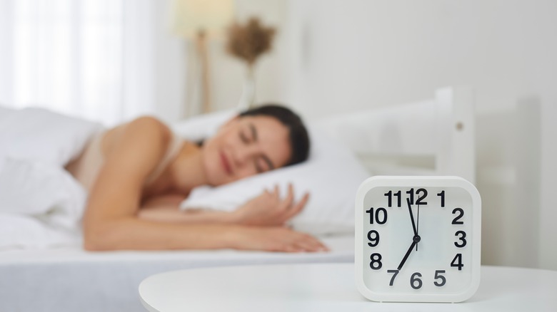 woman in bed sleeping with alarm clock in foreground