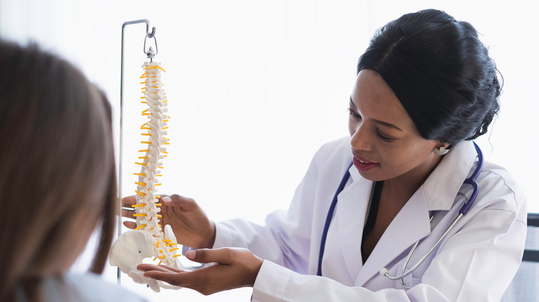A doctor holds up a model spine and explains specific points to her patient