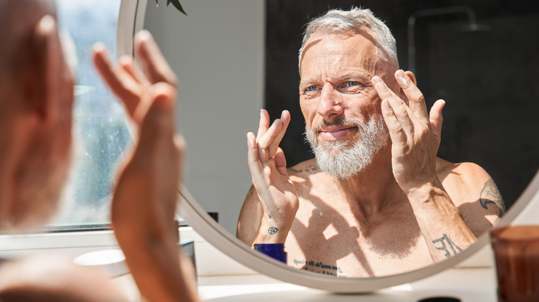 man applying skincare in mirror