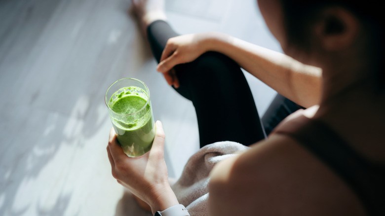 An over-the-shoulder shot of a young woman drinking a green drink